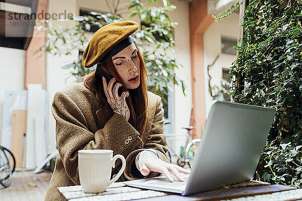 Frau telefoniert und benutzt Laptop im Straßencafé