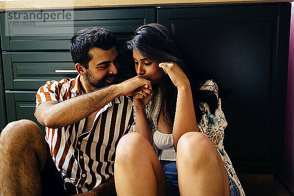 Romantic woman kissing hand of boyfriend sitting at home