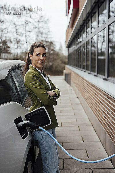 Lächelnde Frau lehnt an Elektroauto mit Ladekabel