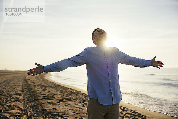 Carefree mature man standing with arms outstretched at beach