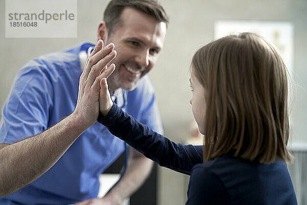 Happy doctor giving high-five to girl in clinic