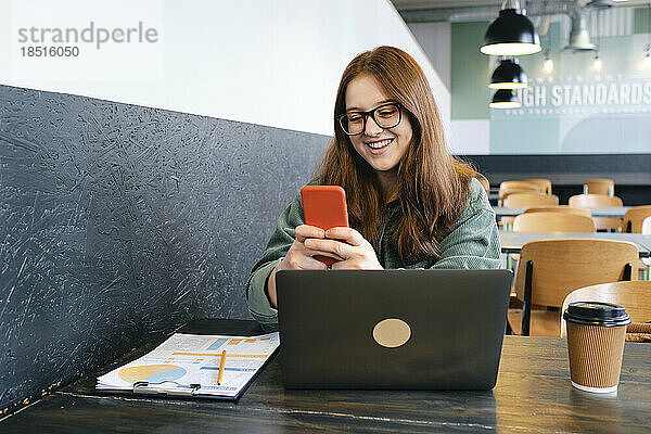 Fröhlicher junger Freiberufler nutzt Smartphone im Café