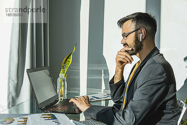 Geschäftsmann mit der Hand am Kinn arbeitet am Laptop im Heimbüro