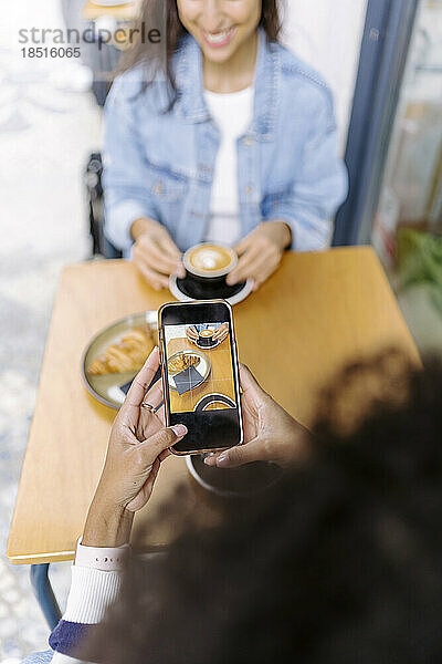 Junge Frau fotografiert Speisen und Getränke per Smartphone