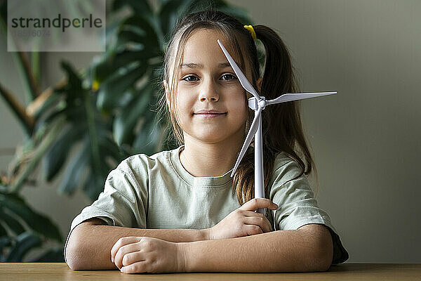 Girl with wind turbine model sitting at table