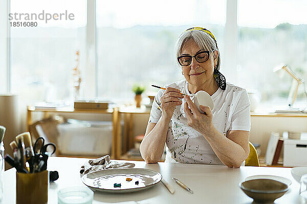 Lächelnde ältere Frau malt Tasse im Studio