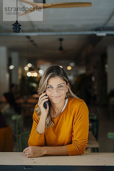 Lächelnde Frau  die im Café über ihr Mobiltelefon spricht