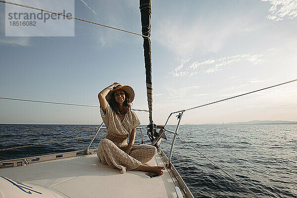 Lächelnde Frau mit Hut sitzt auf einem Segelboot