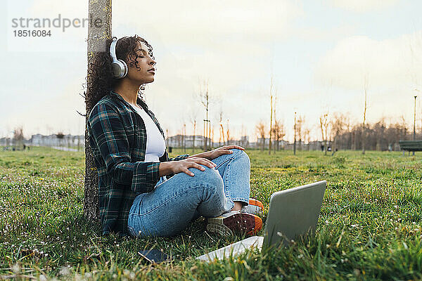 Junge Frau meditiert mit Laptop im Park