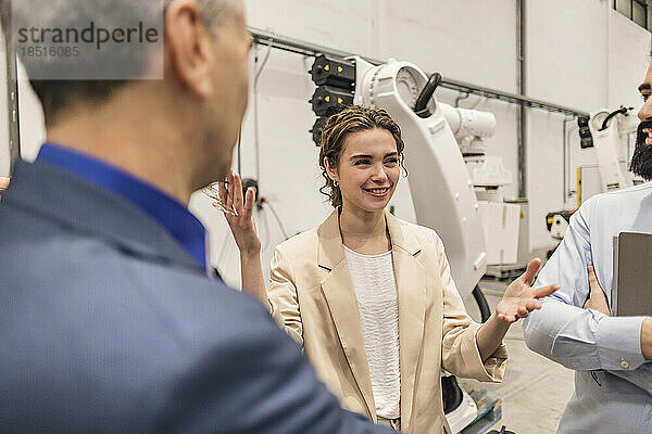 Lächelnder junger Ingenieur gestikuliert und diskutiert in der Fabrik