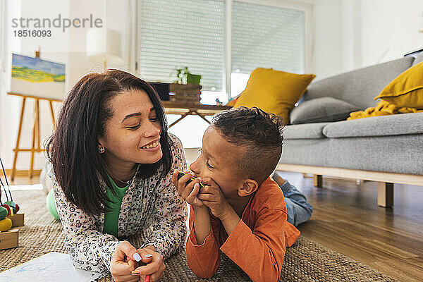 Happy mother and son lying in living room at home