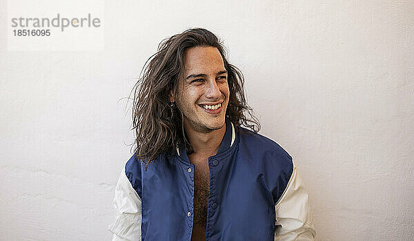 Happy young man with long hair in front of white wall