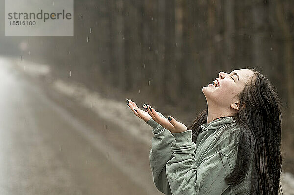 Fröhliches Teenager-Mädchen genießt den Regen auf der Straße