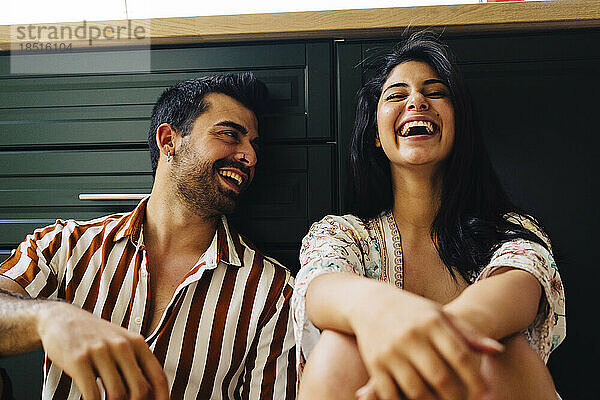 Couple laughing together sitting in front of drawers at home