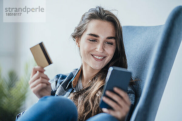 Glückliche Geschäftsfrau benutzt Mobiltelefon und sitzt mit Kreditkarte