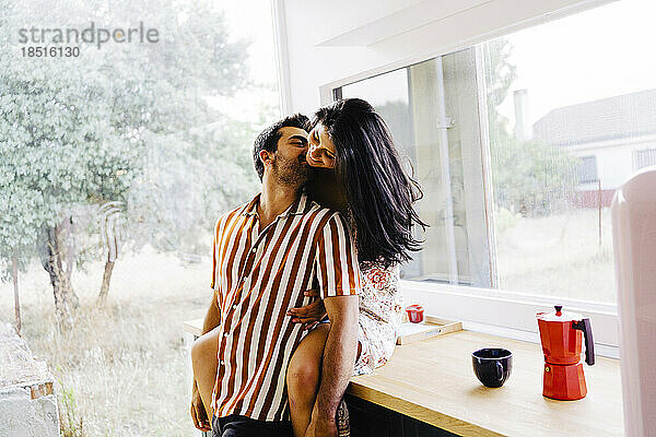 Man kissing girlfriend sitting on kitchen counter at home