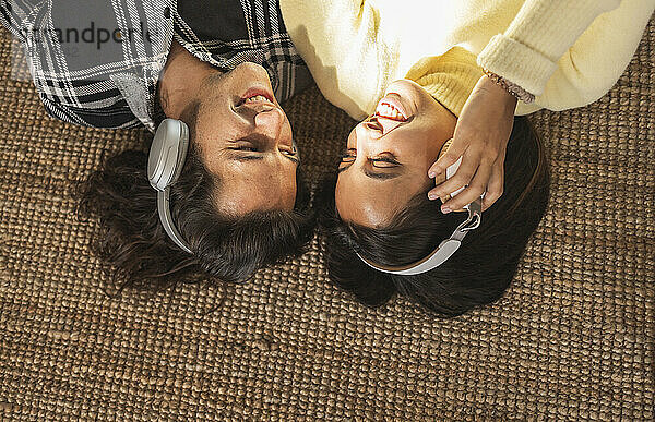 Glückliches Paar hört Musik über Kopfhörer  die auf dem Teppich liegen