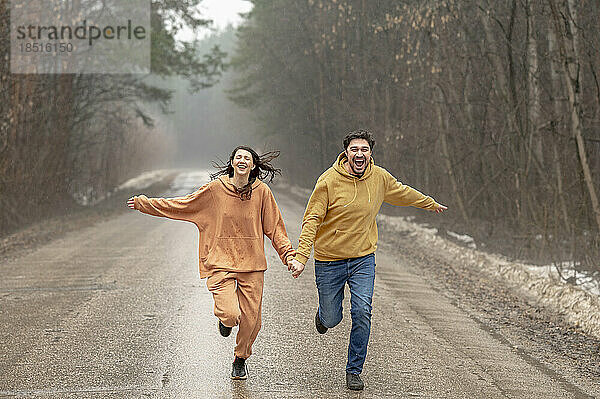Glückliches Paar hält Händchen und läuft auf nasser Straße