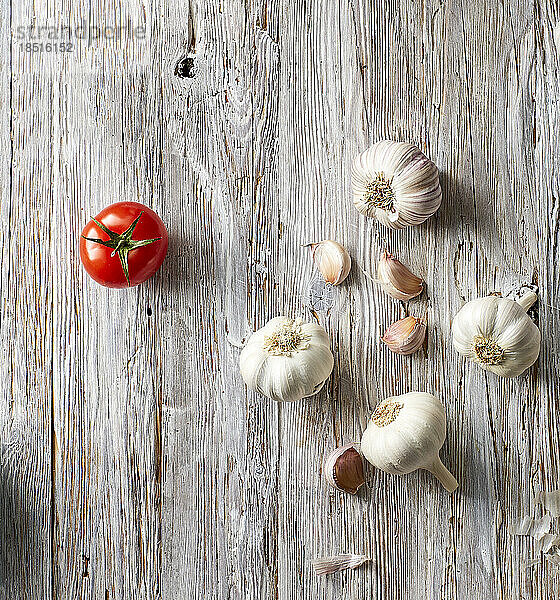 Garlic cloves and single tomato lying on wooden surface