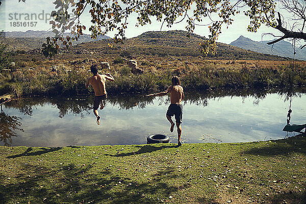 Sorglose Freunde ohne Hemd springen im Urlaub in den See