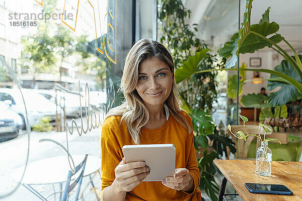 Lächelnde Frau mit Tablet-PC sitzt im Café