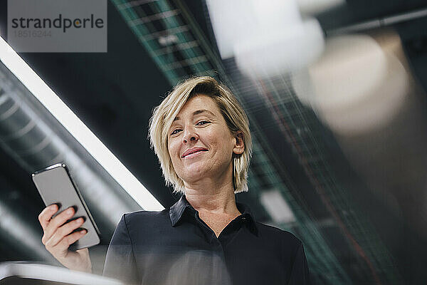 Lächelnde Geschäftsfrau mit Smartphone im Büro