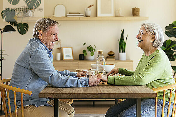 Liebevolles älteres Paar  das Händchen hält und am Esstisch sitzt