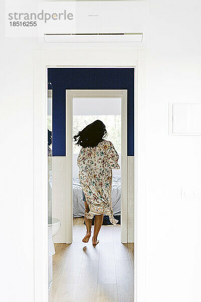Young woman running towards bedroom seen through doorway