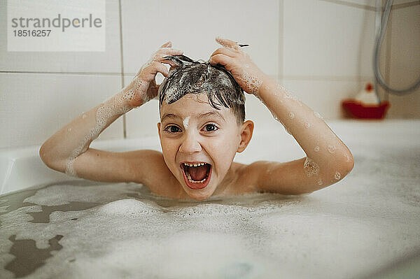 Happy boy having fun in bathtub at home