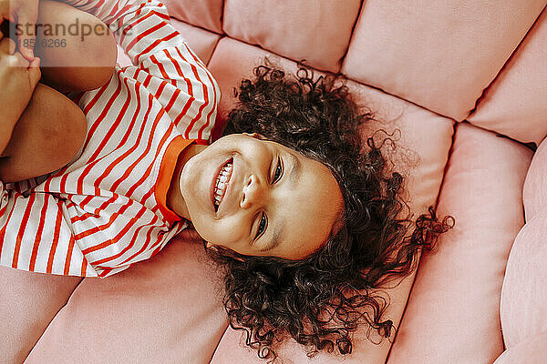 Fröhliches Mädchen  das sich zu Hause auf dem rosa Sofa amüsiert