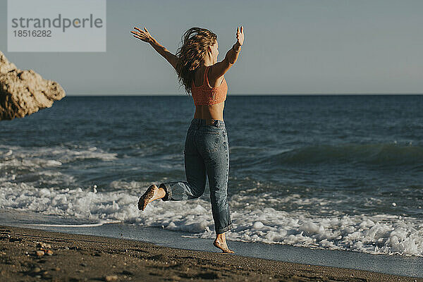 Frau springt an sonnigem Tag vor das Meer