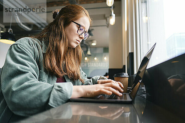 Junger Freiberufler tippt im Café am Laptop