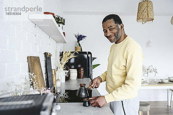 Lächelnder reifer Mann  der zu Hause in der Küche Kaffee zubereitet