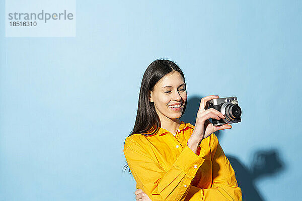 Glückliche junge Frau hält Kamera vor blauem Hintergrund