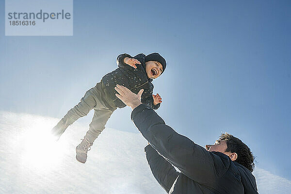 Verspielter Vater wirft Sohn an sonnigem Tag in die Luft