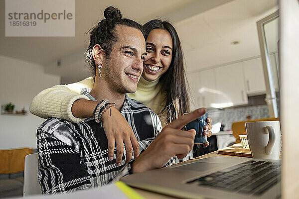 Glücklicher junger Mann diskutiert mit Freundin am Laptop im Heimbüro