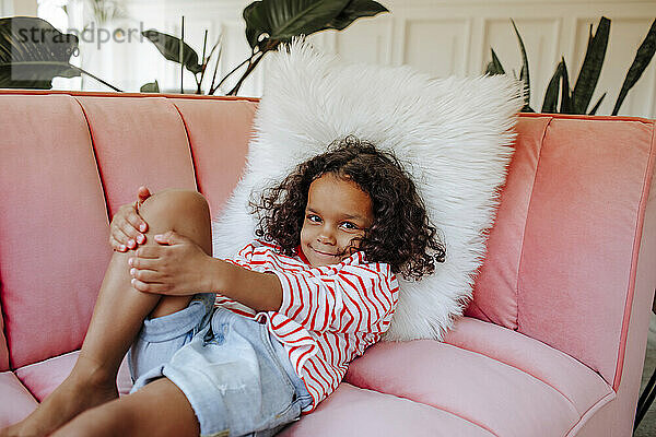 Lächelndes süßes Mädchen  das zu Hause auf rosa Sofa liegt