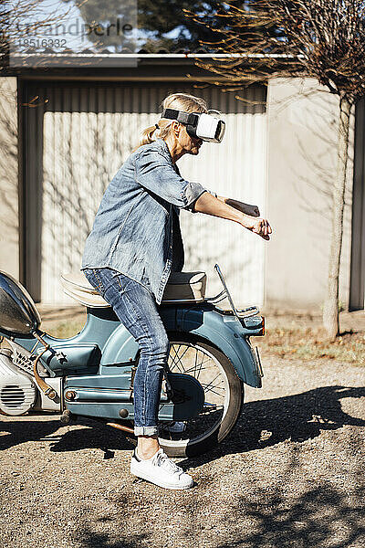 Frau mit VR-Brille gestikuliert auf Motorrad