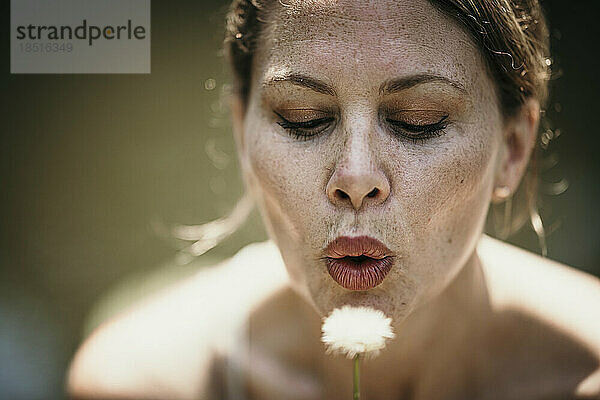 Mature woman blowing dandelion on sunny day