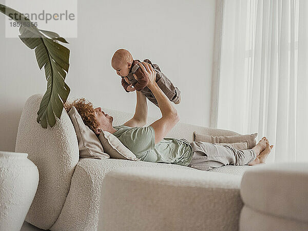 Vater liegt auf Sofa und spielt zu Hause mit Sohn