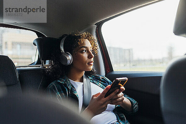 Nachdenkliche Frau mit Smartphone sitzt im Auto