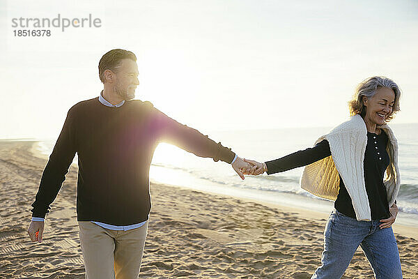 Glückliche Frau hält Händchen mit Mann und hat Spaß am Strand
