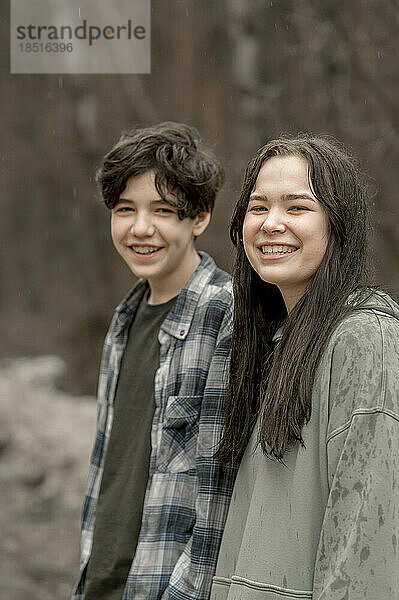 Lächelnde Teenager-Geschwister in Freizeitkleidung an einem regnerischen Tag