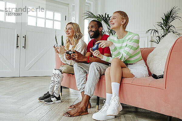 Glücklicher junger Mann spielt Videospiel mit Frauen  die zu Hause auf dem Sofa sitzen