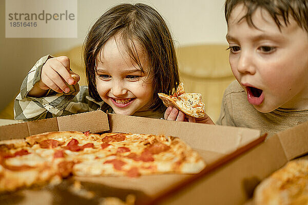 Glücklicher Junge  der zu Hause mit seinem Bruder Pizza isst