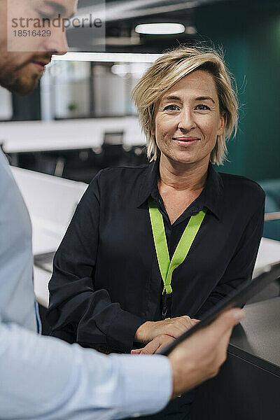 Lächelnde Geschäftsfrau mit Kollege hält Tablet-PC im Büro