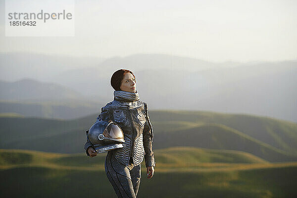 Nachdenkliche Frau mit Weltraumhelm steht auf der Landschaft