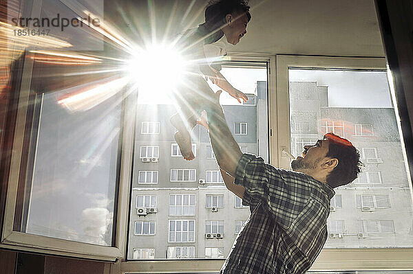 Vater spielt mit Sohn am Fenster an einem sonnigen Tag zu Hause