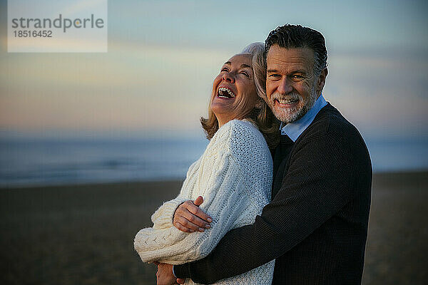 Fröhlicher Mann und Frau umarmen sich am Strand