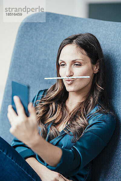 Junge Frau hält Strohhalm über die Lippen und macht ein Selfie